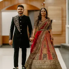 A full-length shot of the couple walking hand in hand, showcasing their stunning reception outfits. The bride's intricate lehenga and the groom's coordinated sherwani make for a grand and stylish wedding portrait.