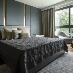 A bedroom featuring a dramatic, floor-to-ceiling upholstered headboard with brass inlay. The dark, moody color palette and geometric-patterned rug create a sophisticated and luxurious feel.
