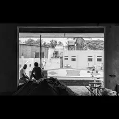 A black and white photograph capturing workers on a construction site, framed by a large window opening, telling the human story behind the architecture.