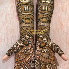 A stunning example of symmetrical bridal mehandi. Both hands are adorned with identical, intricate patterns featuring peacocks, lotuses, and detailed jaali (net) work.