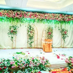 A wide reception stage decorated with a full floral arch of pink and white roses, with hanging floral elements and golden frame accents on a white drape background.
