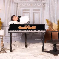 A classic newborn pose, with the baby sleeping on top of the miniature grand piano. The composition is balanced with elegant candlesticks and pampas grass arrangements.