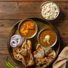 A North Indian thali featuring Chur-Chur Naan, Dal Makhani, and Shahi Paneer for Grover Sweets. The top-down composition on a wooden background creates a wholesome, rustic look.