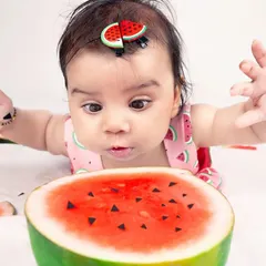 A close-up shot of a baby looking with curiosity at a large slice of watermelon. This image captures a genuine, interactive moment during a themed five-month milestone photoshoot.