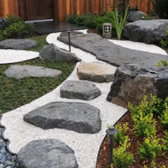 This is a classic Zen garden design featuring a pathway of large, irregular stepping stones set in white gravel. The careful placement of rocks and minimal planting creates a space that encourages contemplation.