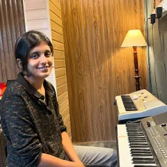 A smiling student sits at the keyboard, ready for her lesson. We offer both online and offline classes at our HSR Layout and Kaggadasapura locations.