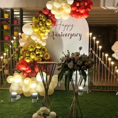 For this anniversary celebration, I used a custom white backdrop with 'Happy Anniversary' script. The decor is accented with a balloon garland in red, gold, and white, along with elegant floral stands.