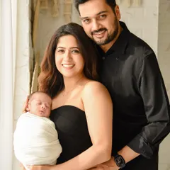 A smiling couple holds their sleeping newborn. This classic family pose beautifully captures the joy and love of the new parents.