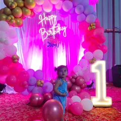 A happy moment from a first birthday party we decorated. The setup includes a custom neon 'Happy Birthday' sign, a balloon arch in pink and gold, and our popular light-up '1' marquee number prop.
