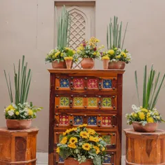 A rustic and charming decor corner for a Jaipur wedding, featuring sunflowers and other yellow blooms arranged in terracotta pots on a traditional tiled chest of drawers.