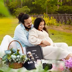 A lovely wide shot of the couple's picnic. The lush green grass and the thoughtfully placed props create a beautiful and relaxed atmosphere for their maternity photos.