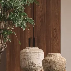 Two large, rustic urns with a weathered, chalky finish stand against a warm wood-paneled wall. Their earthy, grounded presence lends a sense of story without saying a word.