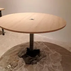 A close-up of a round office discussion table during installation, showing the wooden top and sturdy metal base.