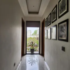 In this hallway, we created a direct axis to the outdoors. The passage terminates with a full-length glass door, drawing the eye towards the greenery and flooding the corridor with natural light, making the space feel open and connected.