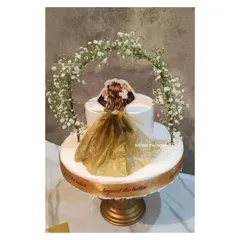 This stunning two-tier "Bride to be" cake is perfect for a sophisticated celebration. It features a custom illustration of the bride, a real fabric dress detail, and a beautiful arch of fresh baby's breath.