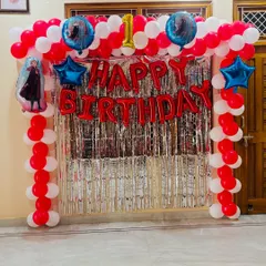 A Frozen-themed first birthday party decoration. This setup has a red and white balloon arch with characters from the movie and a silver shimmer curtain.