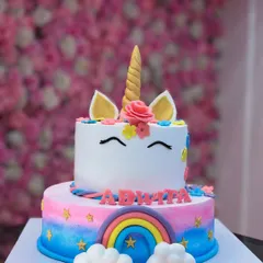 A two-tiered unicorn cake with a rainbow on the bottom tier and a cute unicorn face on top. The fondant clouds and stars complete this enchanting design.