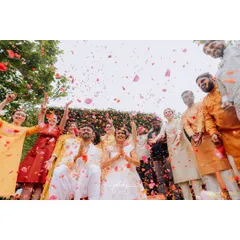 A moment of pure joy during a Haldi ceremony, as guests shower the couple with a cascade of flower petals. The dense floral wall in the background makes the colors pop.