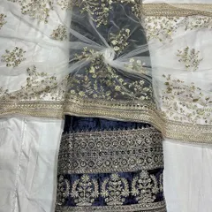 This deep navy blue velvet fabric is paired with a delicate white net dupatta. The gold embroidery on both fabrics is designed to coordinate perfectly for a complete, luxurious outfit.