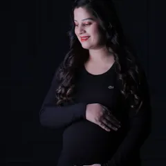 A beautiful low-key portrait. The soft light illuminates one side of the mom-to-be's face and her baby bump, creating a gentle, moody, and artistic photograph.