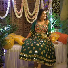 The bride-to-be enjoying her Mehendi function. The backdrop here is a traditional carved wooden panel, softened with beautiful garlands of white and pink flowers. The yellow cushions add a bright pop of color, creating a perfect blend of traditional and festive decor.