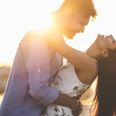 A sun-drenched, joyful moment as a couple embraces on the beach, with the golden hour light creating a beautiful flare and highlighting their laughter.