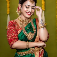 A beautiful bride glowing with happiness. She is wearing a classic temple jewellery set with green and red stones, perfectly matching her green and red silk saree.