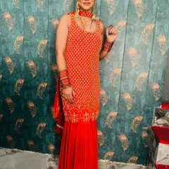 A full-length photo of a happy client in a red sharara suit, perfect for a wedding party.