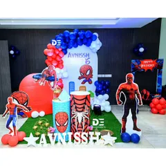 A cool Spiderman setup for Avnissh's 6th birthday. This decor includes a cityscape backdrop, multiple Spiderman cutouts in different poses, and a red, white, and blue balloon arch.