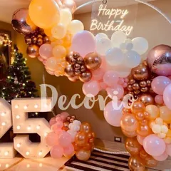 This birthday setup features a circular ring frame decorated with a pastel and rose gold balloon garland. The 'Happy Birthday' neon sign and '25' marquee numbers complete this popular and trendy decor style.