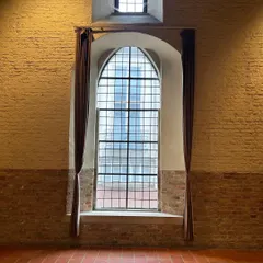 A magnificent arched window inside the Belfort Museum in Bruges. The scale of the window, combined with the exposed brick wall and terracotta floor, creates a powerful sense of history and space.