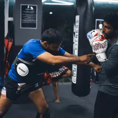 A coach points out a target during a pad work session. This drill sharpens a fighter's accuracy and teaches them to aim for effective scoring areas.