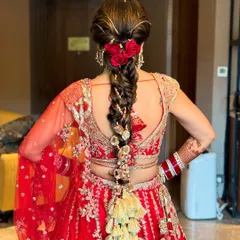 This is a quintessential Indian bridal look, featuring a thick, traditional braid adorned with red roses and intricate gold tassels (parandi). This hairstyle is designed to perfectly match a classic red lehenga, making it ideal for the main wedding ceremony.