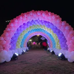 A rainbow balloon arch tunnel in a garden, creating a fairytale entrance for a princess-themed birthday party.