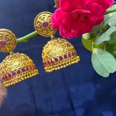 Classic temple jewellery style jhumkas. These gold earrings with intricate heart motifs and red stones are a timeless accessory.