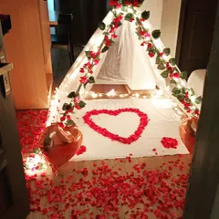 This romantic canopy tent is one of my popular offerings for an intimate celebration. I use a sheer white tent, wrap it in fairy lights and red flower vines, and create a heart shape with rose petals on the floor inside.