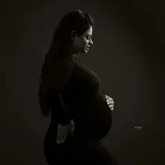 A classic low-key portrait in black and white. The lighting is carefully shaped to sculpt the client's form, creating a timeless and intimate image that focuses on the beauty of her pregnancy.