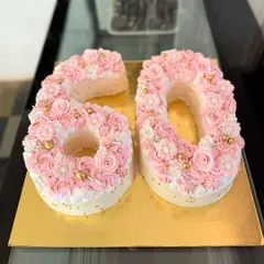 Celebrating a 60th birthday in style with a beautiful monogram cake. Each number is delicately decorated with pink and white buttercream flowers and shimmering gold sprinkles for an elegant and personal touch.