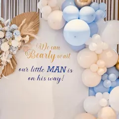 The details make the difference. This close-up shows the custom vinyl text "We can Bearly wait, our little MAN is on his way!" on a clean white backdrop, framed by a balloon garland and dried floral accents for a rustic touch.