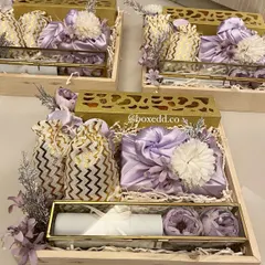 A stunning wedding invitation hamper designed with a lavender and gold theme. These wooden trays include a scroll invitation in a glass box, furoshiki-wrapped gifts, and sweet pouches, creating a truly luxurious experience for your guests.