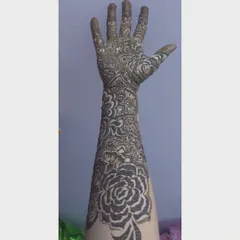 A clear view of a full arm bridal mehendi design while the paste is still on. This style features a prominent rose on the forearm, a classic choice for modern brides.