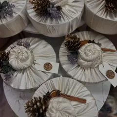 A close-up of Furoshiki-style fabric wrapping on round boxes. I teach how to create these beautiful fabric knots and finish them with custom wax seals and natural adornments like cinnamon sticks and dried oranges.