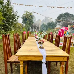 A long wooden dining table set up outdoors with simple, elegant floral centerpieces, ready for a family-style meal.