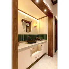A modern and rustic vanity corner in a passage area. The design combines a stone-carved basin with a sleek, irregularly shaped backlit mirror and warm wood tones.