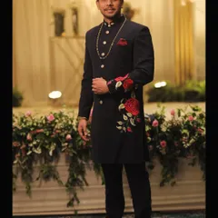 We blend tradition with modern artistry. This bespoke navy sherwani features intricate red rose embroidery, creating a standout piece for any grand occasion. Our expertise in traditional Indian menswear ensures you look regal and unique.