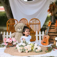 This shot captures the baby girl looking off to the side with a happy expression. The full birthday setup with rustic and floral elements provides a beautiful backdrop for her first birthday portraits.