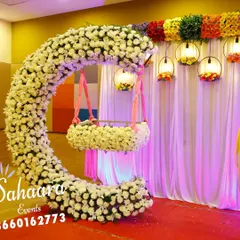 A stunning cradle ceremony setup featuring a crescent-shaped arch made of white flowers. The hanging cradle, also adorned with flowers, creates a beautiful focal point, while colorful lanterns add a festive touch.