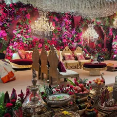 Another angle of the red and pink floral cave stage, showing the intricate details of the seating arrangement and the offering platters. The high-backed chairs and velvet cushions add to the royal feel.