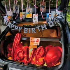 Combining love and birthdays in one surprise. This car dikki decoration features a "Happy Birthday" banner, hanging personal photos, and large red foil balloons spelling out "love" for a heartfelt and personalized message.