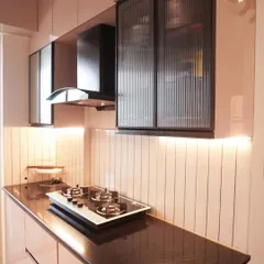 A charming parallel kitchen with soft pink glossy cabinets and a black granite countertop. The design is complemented by a vertically tiled backsplash and under-cabinet lighting, creating a warm and inviting space.